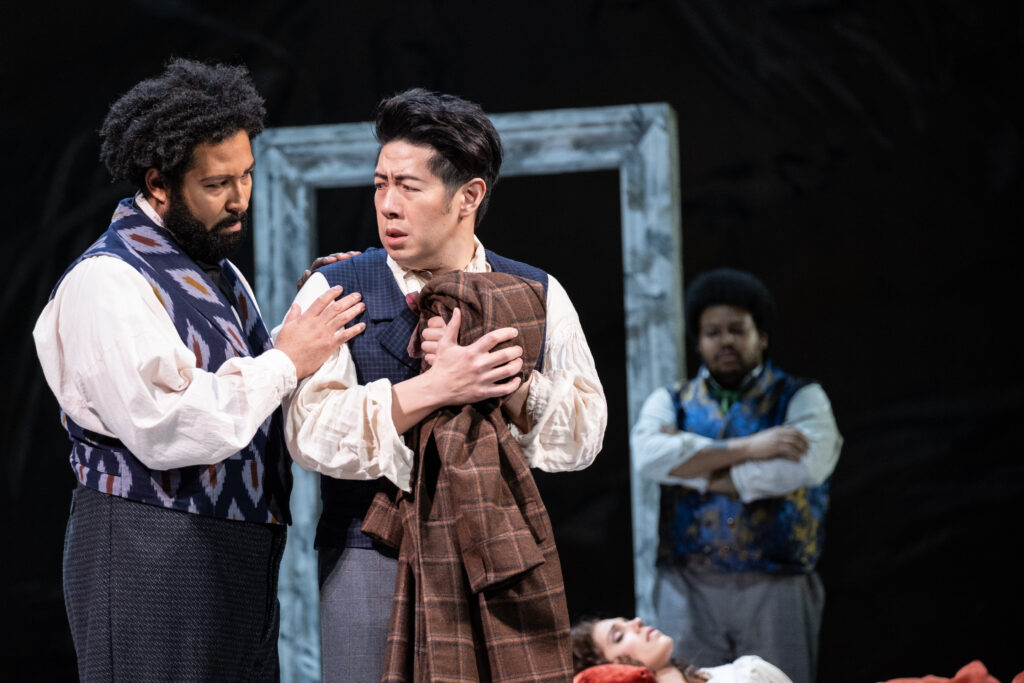Schaunard (Benjamin Taylor) comforts Colline (Adam Lau) who ponders selling his beloved coat to get medicine for a sick Mimì. Photo by Ray Bailey.